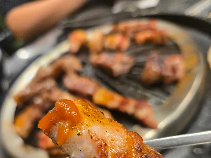 맛있게 구워진 흑돼지 한 점을 젓가락으로 집어 올리는 모습