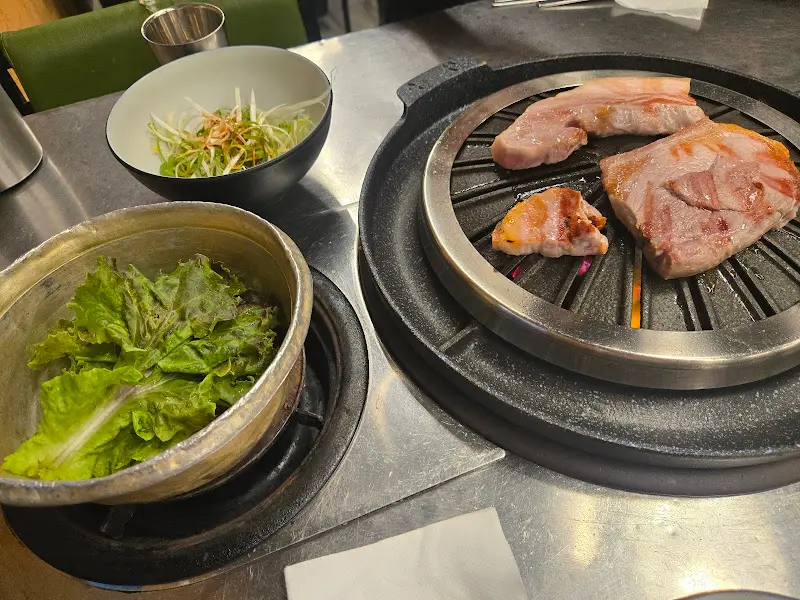 불판 위에 삼겹살과 야채가 함께 구워지고 있는 모습