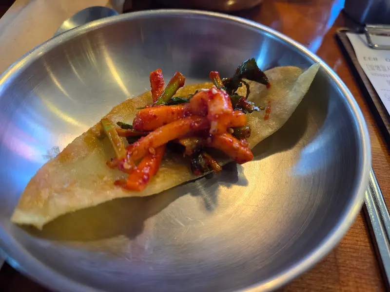 납작만두에 무침회를 싸서 은색 그릇에 담은 모습