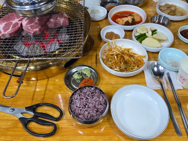 숯불 위에 구워지고 있는 목살과 주변 반찬들의 모습