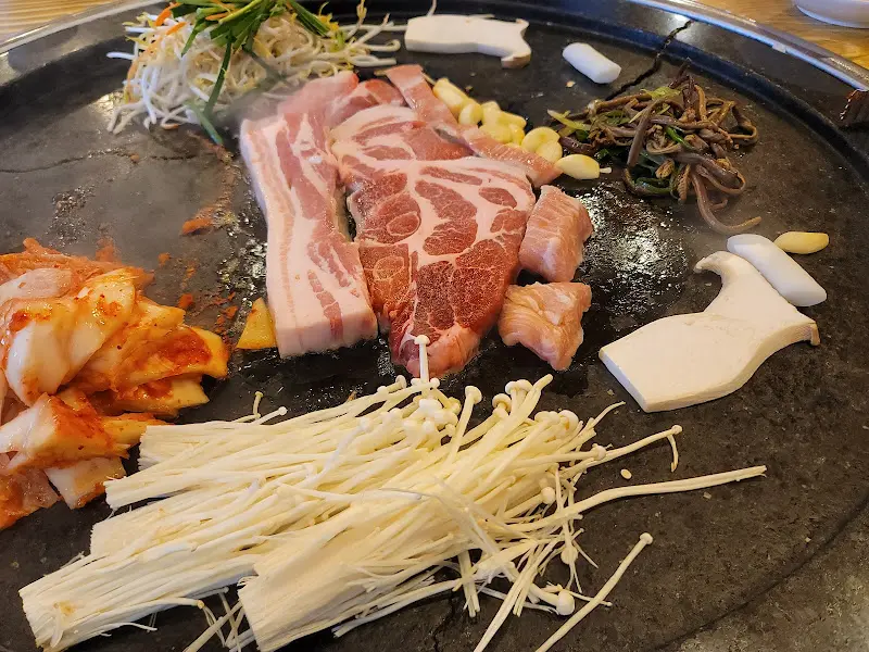 돌판에 삼겹살, 김치, 콩나물, 고사리, 버섯 등이 푸짐하게 구워지고 있는 모습