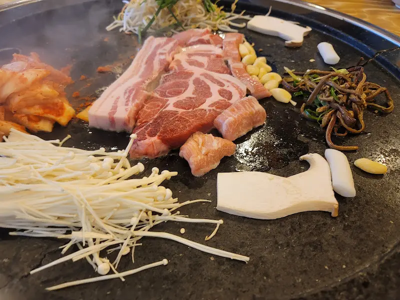 돌판 위에 삼겹살, 김치, 버섯 등이 구워지고 있는 모습
