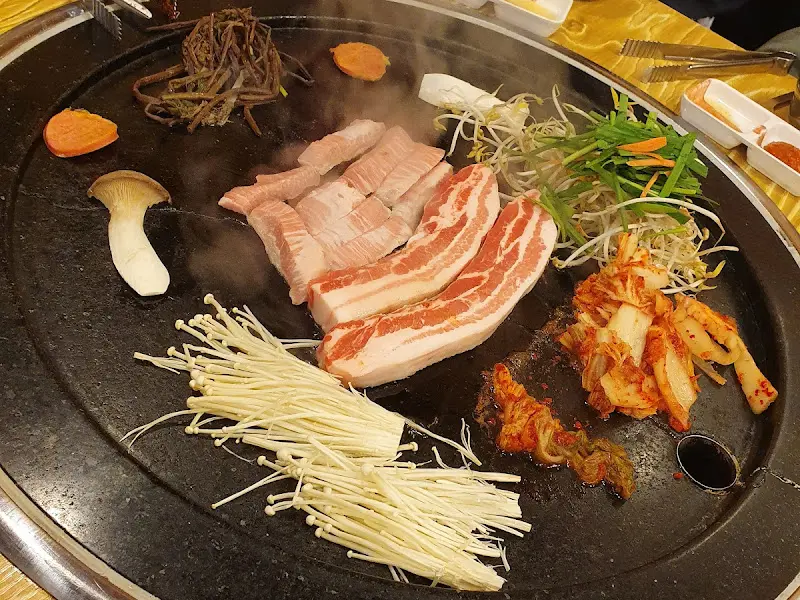 돌판 위에 삼겹살과 다양한 채소들이 구워지고 있는 모습