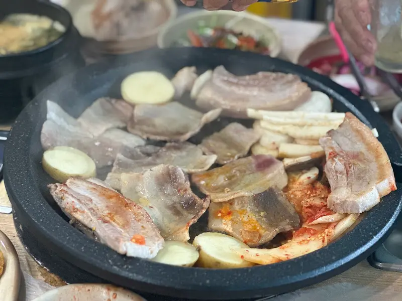 돌판 위에 삼겹살, 김치, 버섯 등이 함께 구워지는 모습