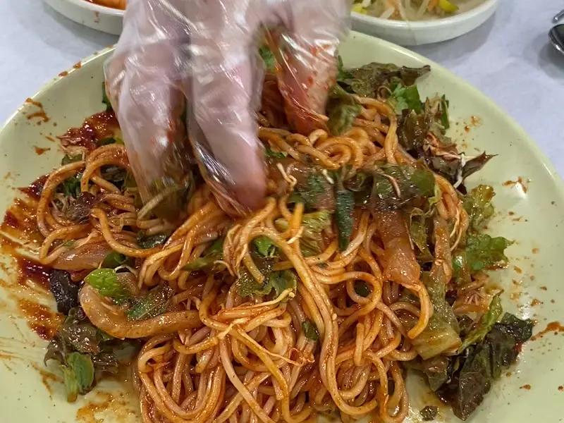 비닐장갑을 끼고 회국수를 비비는 모습. 양념이 면에 골고루 잘 배어있다.