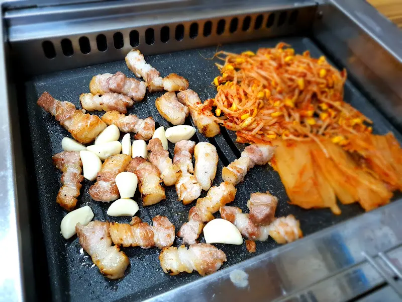 불판 위에서 익어가는 삼겹살과 김치, 콩나물