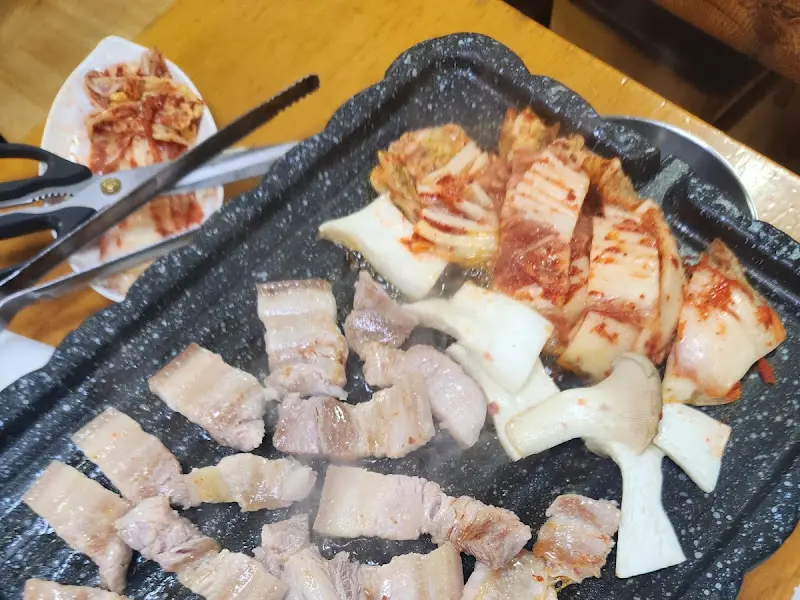 잘 구워진 삼겹살과 김치가 불판 위에 놓여 있는 모습