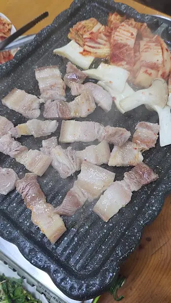 불판 위에 삼겹살, 김치, 버섯이 함께 구워지고 있는 모습