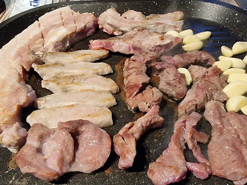 불판 위에서 맛있게 익어가는 삼겹살과 마늘