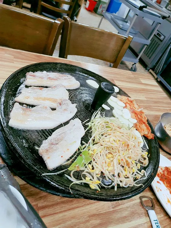 솥뚜껑에 구워진 삼겹살과 김치, 콩나물