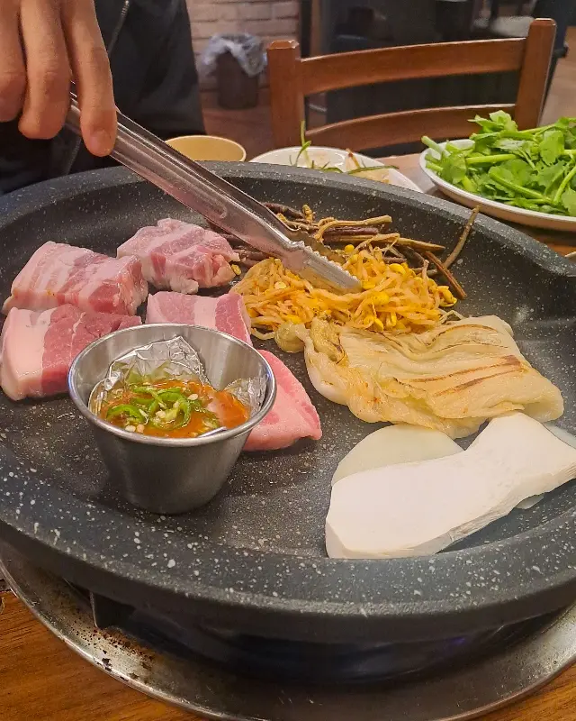 오겹살을 멜젓에 찍어 콩나물, 김치와 함께 쌈을 싸 먹는 모습