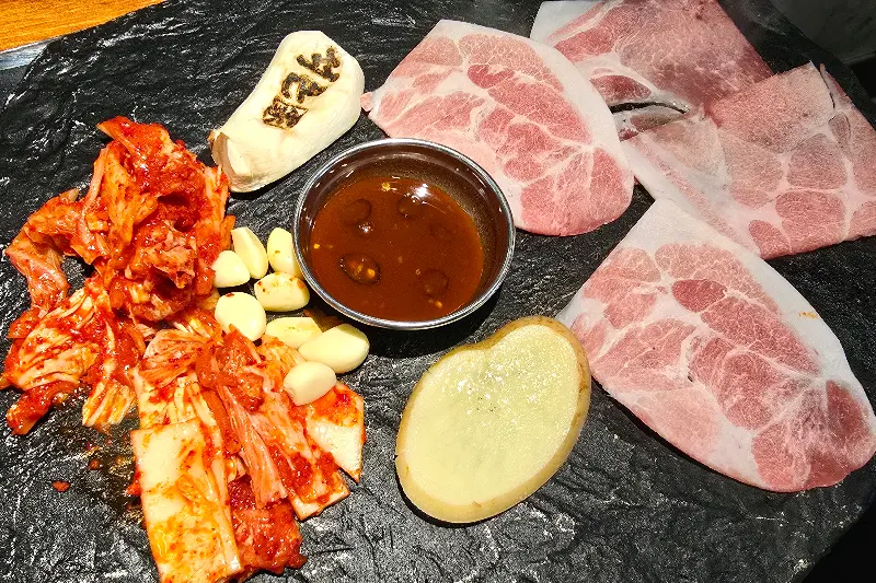 돌판 위에 삼겹살, 김치, 마늘 등이 올려져 있는 모습