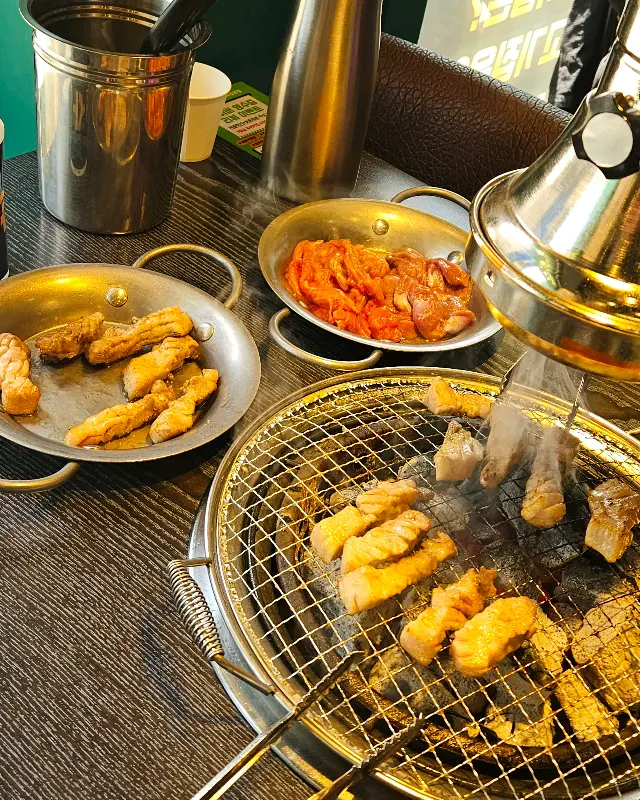 초벌된 삼겹살과 닭목살이 숯불 위에서 맛있게 익어가는 모습