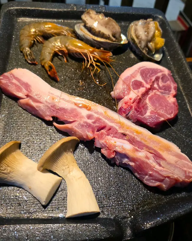 불판 위에 올려진 흑돼지 오겹살, 목살, 전복, 새우