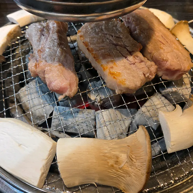숯불 위에서 익어가는 삼겹살과 버섯