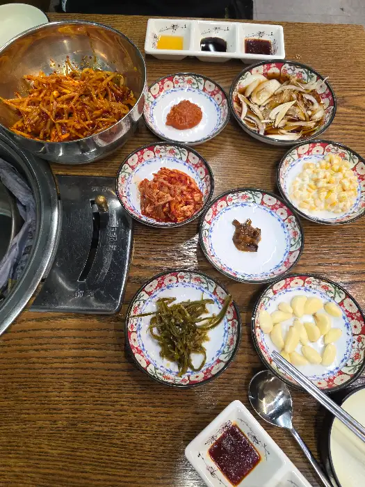 다양한 종류의 밑반찬들이 여러 개의 작은 접시에 정갈하게 담겨 테이블을 채우고 있다. 한국적인 아름다움이 느껴진다.