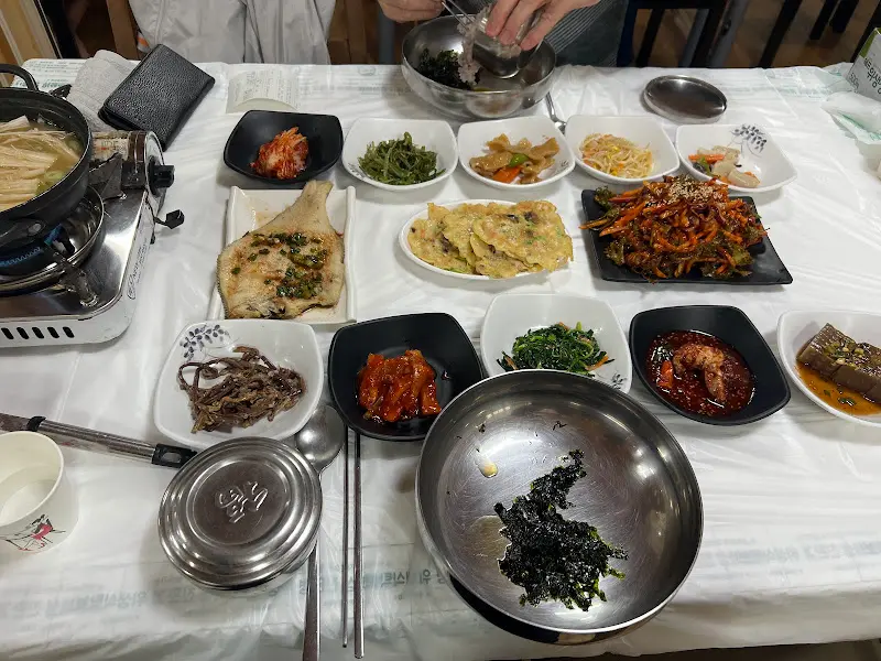 다양한 반찬과 꼬막 요리들이 테이블을 가득 채운 모습. 푸짐한 양이 인상적이다.