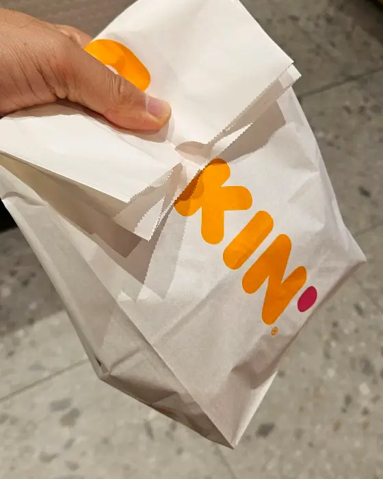 오렌지색 로고가 새겨진 흰색 쇼핑백을 들고 있는 손을 보여주는 사진
