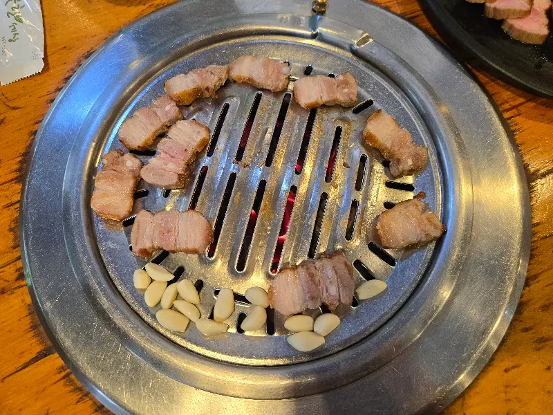 불판 위에 올려진 돼지고기 주변으로 마늘이 함께 구워지고 있는 모습