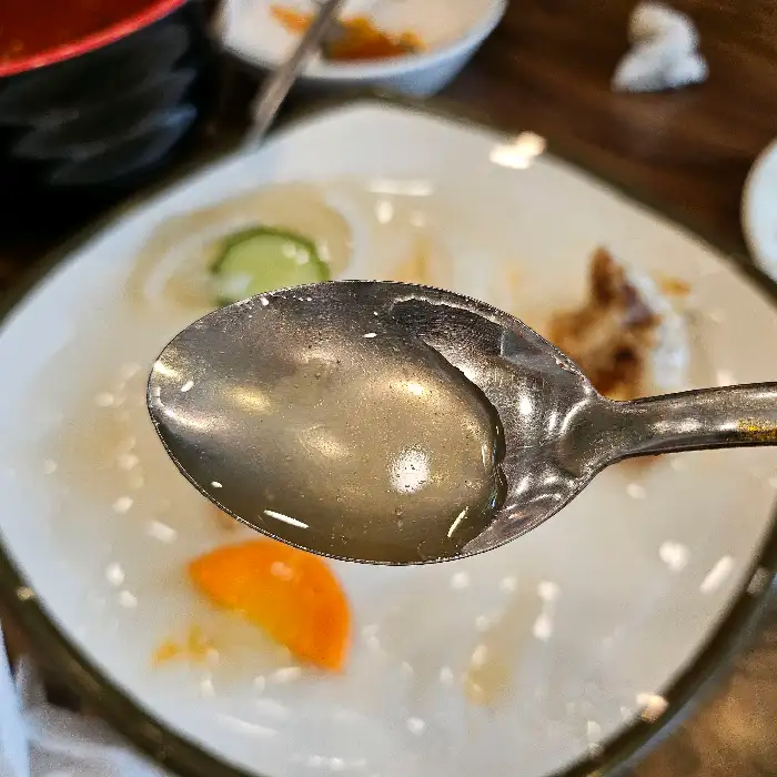 숟가락에 담긴 짬뽕 국물, 그릇 안에는 몇 조각의 고기와 채소, 오징어가 보인다.