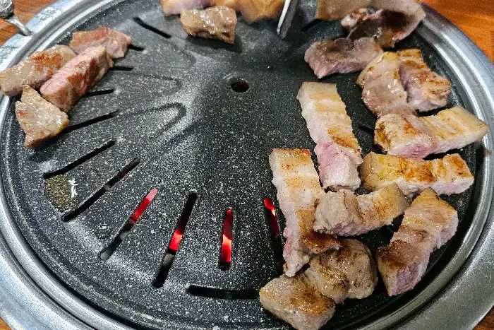동그란 불판 위에 여러 조각으로 나뉜 돼지고기가 구워지고 있는 모습