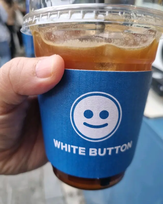 화이트버튼 로고가 새겨진 컵홀더가 씌워진 아이스 아메리카노