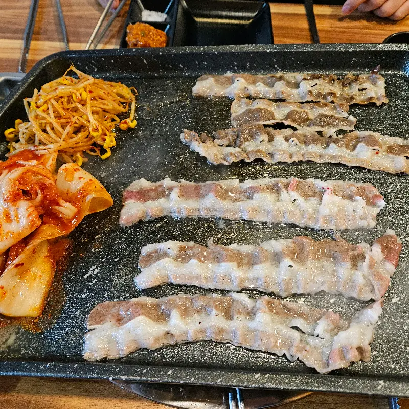 불판에 삼겹살, 김치, 콩나물이 함께 구워지는 모습