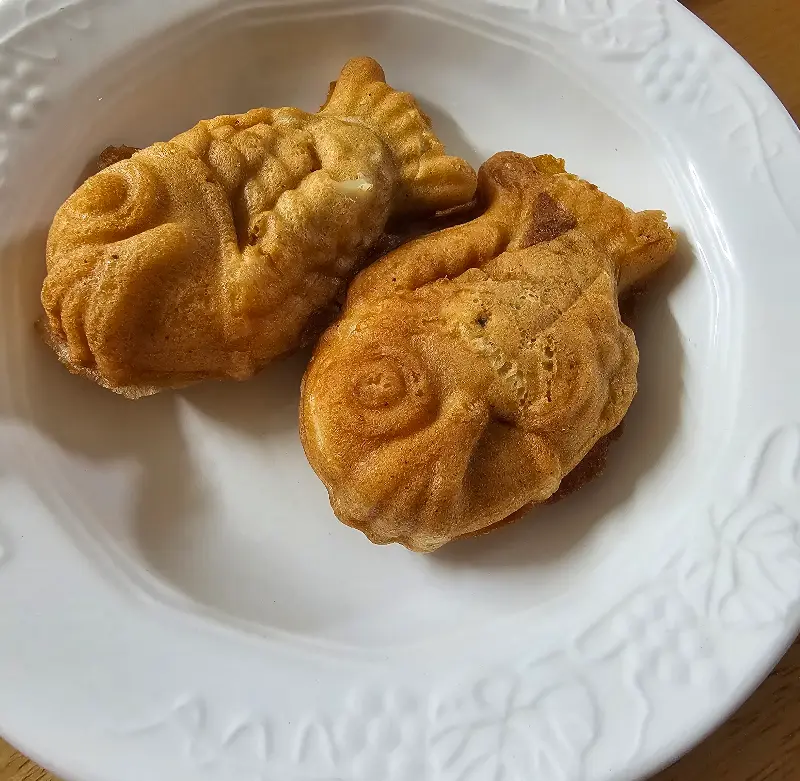 앙증맞은 크기의 미니 붕어빵 두 마리가 흰 접시에 담겨 있는 모습