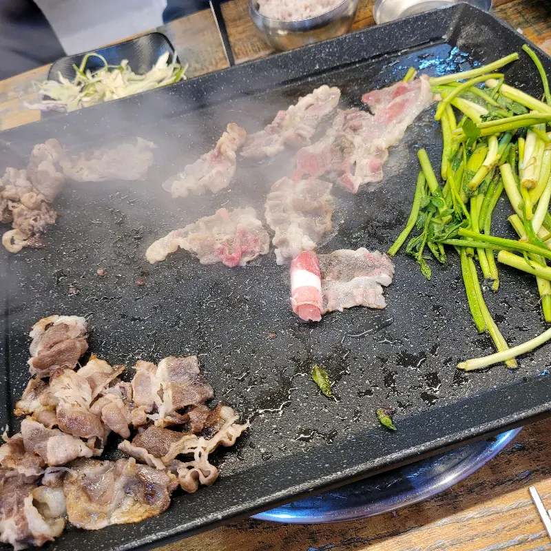 불판 위에서 익어가는 대패삼겹살과 미나리