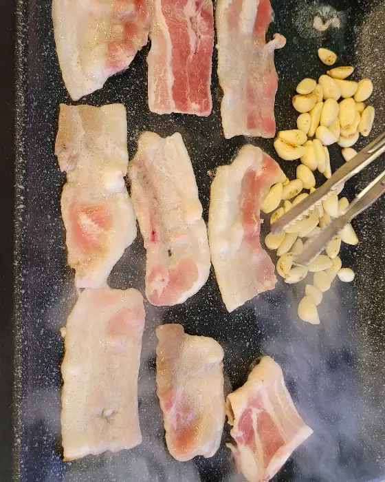 불판 위에서 익어가는 두툼한 고기와 마늘