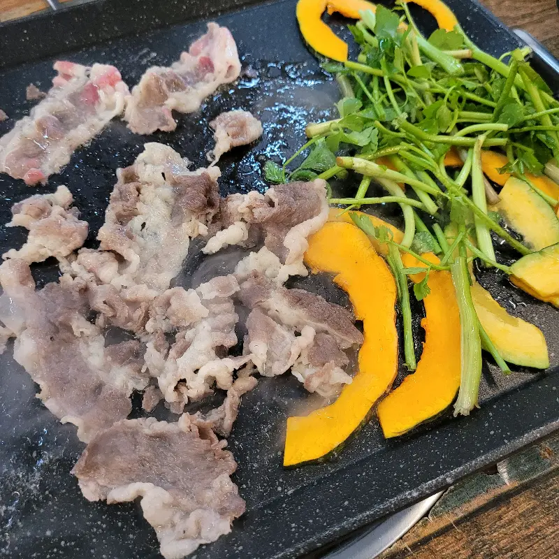 불판 위에서 대패삼겹살과 함께 구워지고 있는 단호박과 미나리