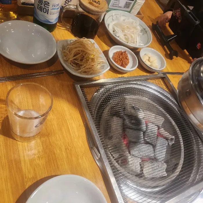 식탁 위에 숯불, 쌈 채소, 양념장, 얇게 썬 양파 등이 놓여 있습니다.