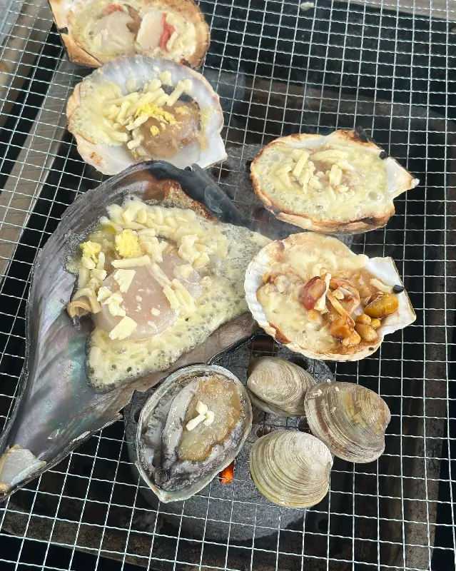 불판 위에서 맛있게 익어가는 조개구이. 치즈와 소스가 어우러져 군침을 돌게 한다.