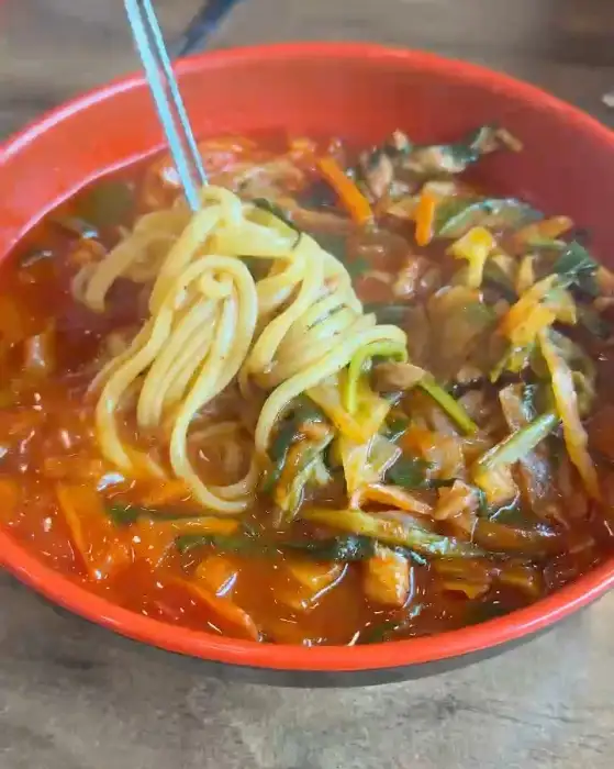 빨간 짬뽕 국물 안에서 젓가락으로 면발을 건져 올리는 모습