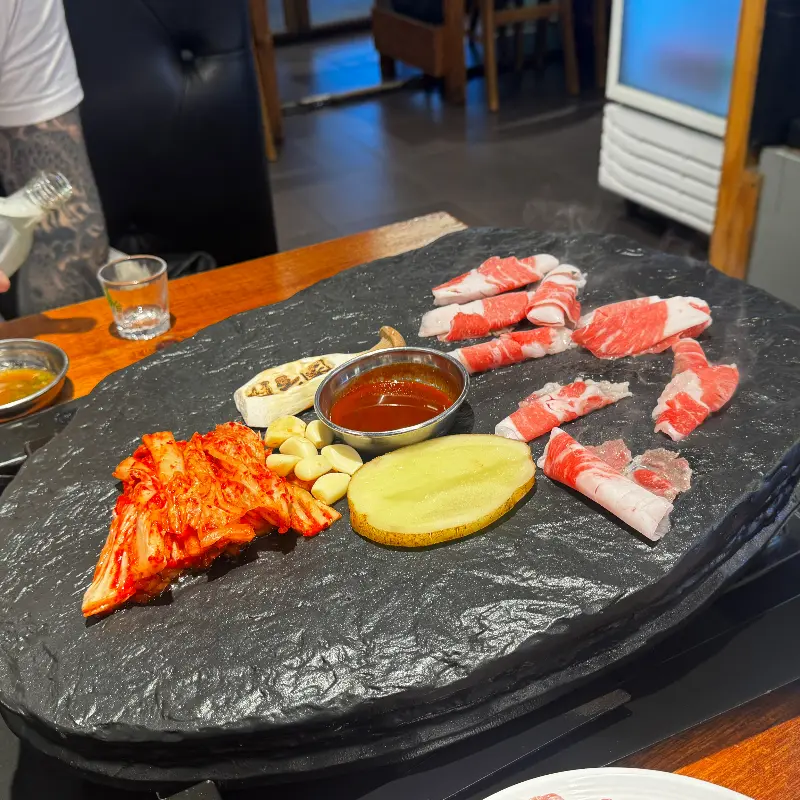 돌판 위에 올려진 얇게 썰린 고기, 김치, 마늘