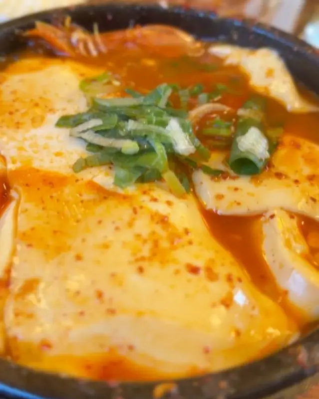 해물 순두부 찌개가 담긴 검은 뚝배기 클로즈업 사진. 큼지막한 순두부와 파, 고춧가루가 보인다.