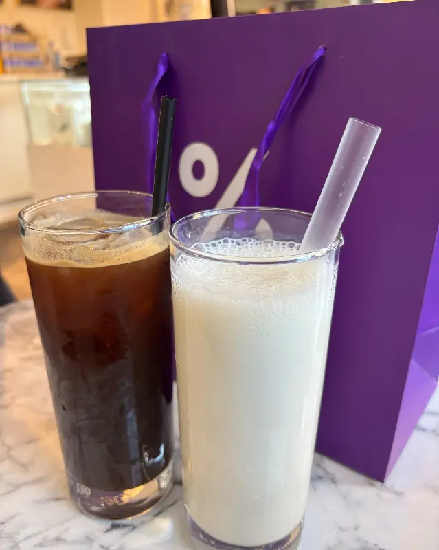 음료 두 잔이 보라색 쇼핑백 옆에 놓여 있는 모습