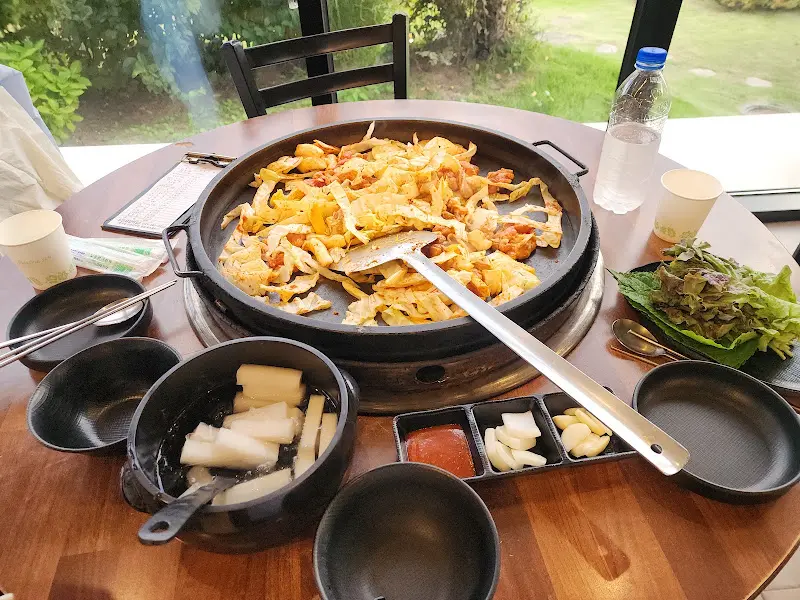 닭갈비 한 상 차림 사진. 닭갈비, 동치미, 쌈 채소 등이 테이블 위에 놓여 있다.