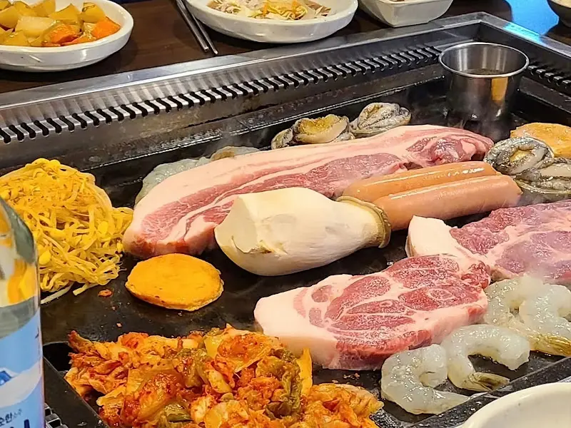 흑돼지 오겹살과 다양한 구이 재료들이 불판 위에서 익어가는 모습