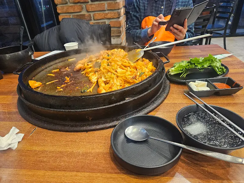 닭갈비가 익어가는 모습. 붉은 양념이 닭고기와 야채에 골고루 스며들어 먹음직스러운 비주얼을 자랑한다. 철판에서 피어오르는 김이 식욕을 자극한다.