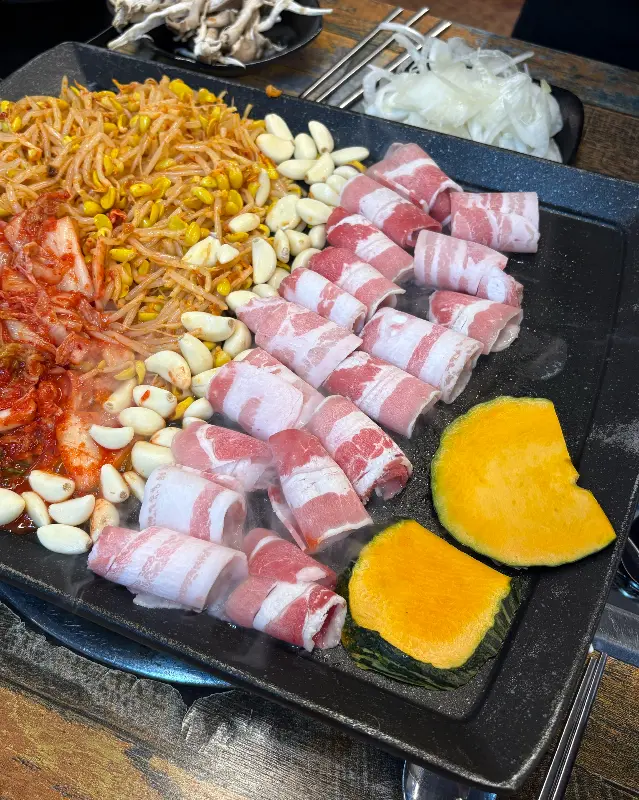 대패삼겹살과 김치, 콩나물, 마늘, 단호박 등이 함께 구워지고 있는 불판