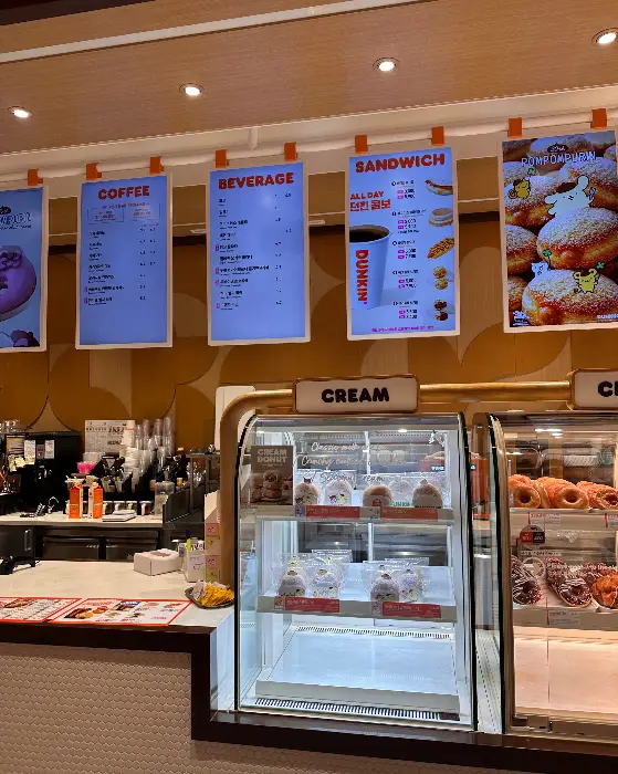 커피, 샌드위치, 도넛 등 메뉴판과 함께 디저트 진열대를 보여주는 사진