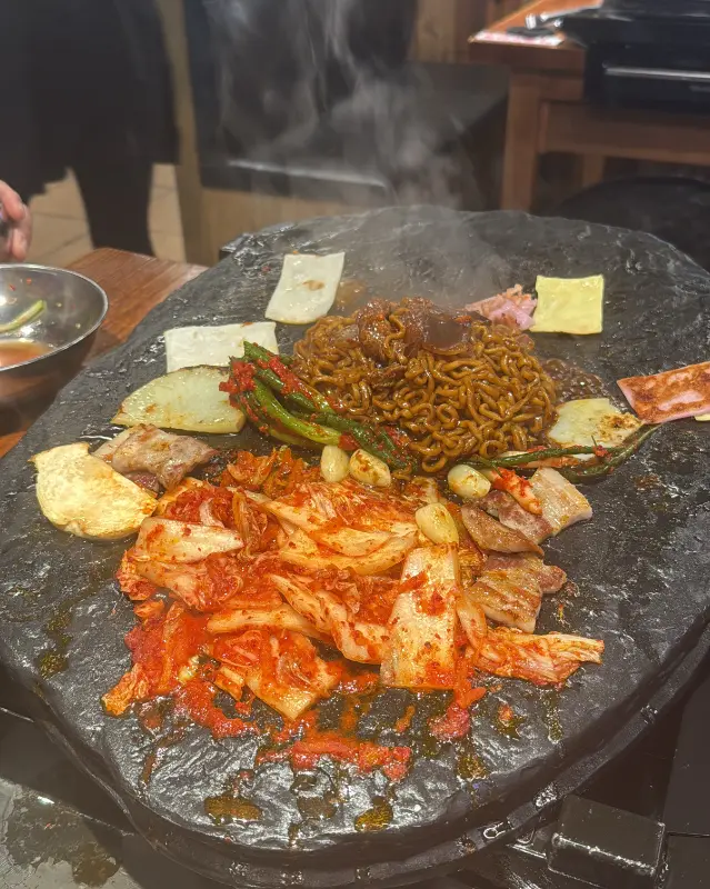 돌판 위에 짜파게티, 김치, 삼겹살, 마늘 등이 함께 올려져 있는 모습