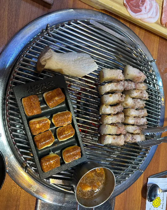 불판 위에 흑돼지 오겹살과 함께 구워지고 있는 멜젓과 구워 먹는 치즈가 보인다.