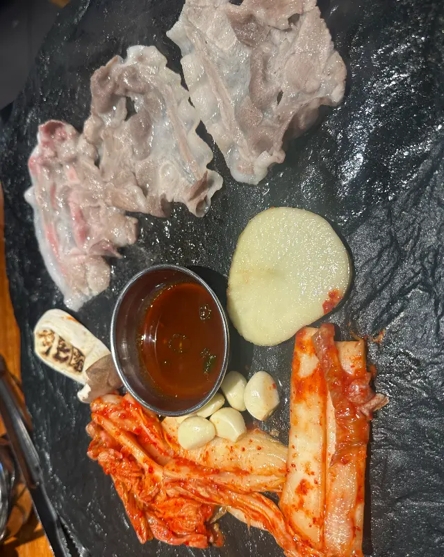 돌판 위에 목삼겹 로스와 김치, 통마늘이 함께 구워지는 모습