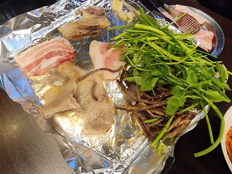 불판 위에서 익어가는 냉삼과 미나리, 고사리