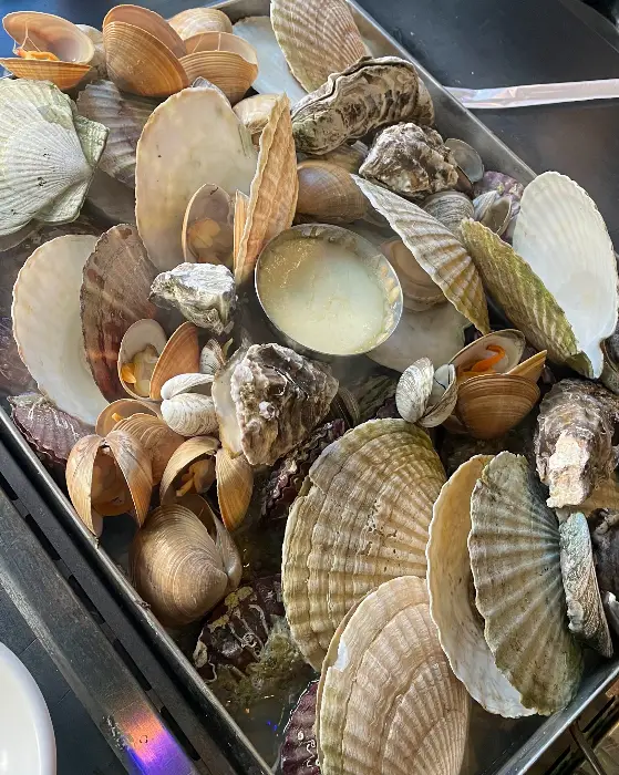 철판 조개 모듬찜에 담긴 다양한 조개와 야채들