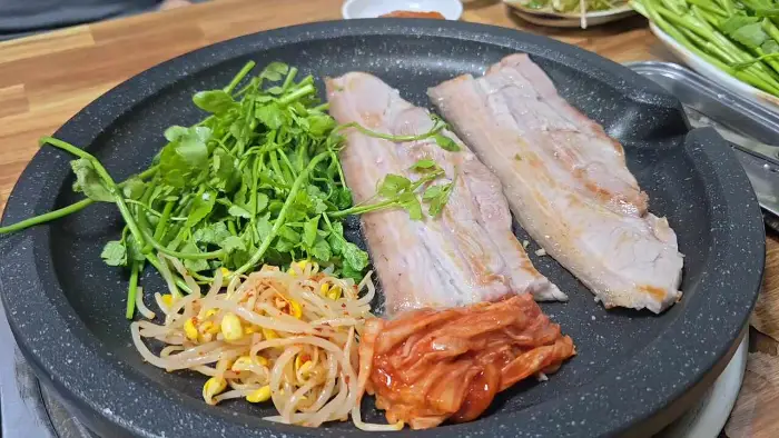 불판 위에 구워지는 삼겹살과 채소 이미지