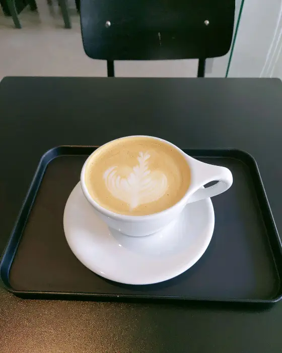 흰색 잔에 담긴 라떼 아트 커피가 놓인 트레이