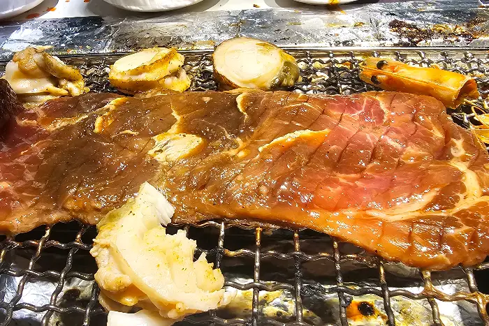 숯불 위에서 구워지는 두툼한 소고기와 조개